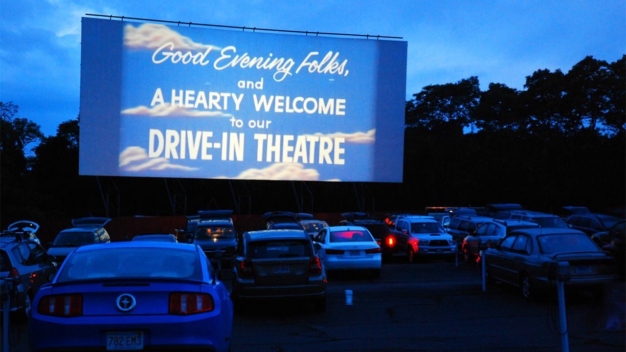 žmonės žiūri filmus įvažiuojamajame kino teatre, o garsas sklinda iš jų automobilių vidaus